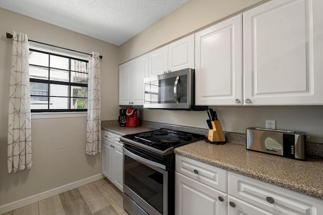15 Cypress St Unit 268, Santa Rosa Beach, FL 32459 - kitchen with stainless steel appliances, light wood finished floors, white cabinetry, a textured ceiling, and baseboards