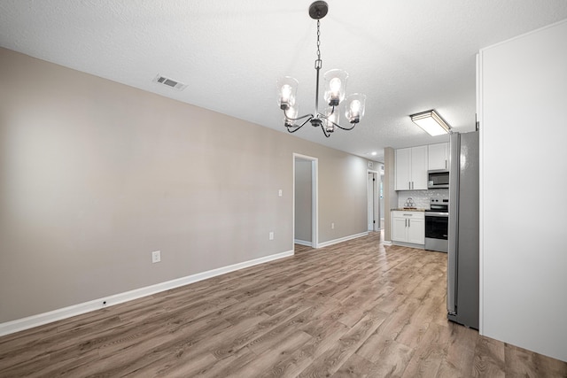 207 Oglesby Ave, Crestview, FL 32536 - kitchen featuring appliances with stainless steel finishes, light wood-type flooring, a chandelier, white cabinetry, and light countertops