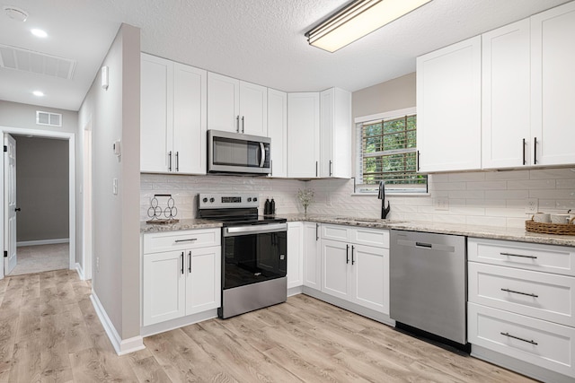 207 Oglesby Ave, Crestview, FL 32536 - kitchen featuring stainless steel appliances, light wood-style flooring, light stone countertops, white cabinets, and decorative backsplash
