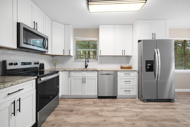 207 Oglesby Ave, Crestview, FL 32536 - kitchen featuring stainless steel appliances, white cabinetry, backsplash, light wood-style flooring, and a textured ceiling