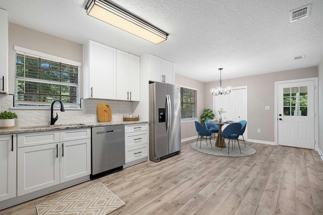 207 Oglesby Ave, Crestview, FL 32536 - kitchen with stainless steel appliances, a chandelier, tasteful backsplash, light wood-style floors, and a textured ceiling
