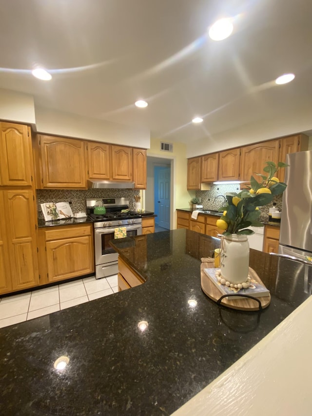22 10th St, Shalimar, FL 32579 - kitchen featuring appliances with stainless steel finishes, under cabinet range hood, decorative backsplash, dark stone counters, and brown cabinetry
