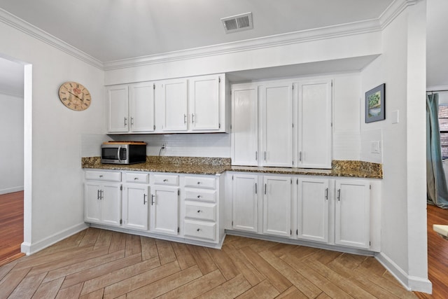 207 Oakwood Cir, Niceville, FL 32578 - kitchen with stainless steel microwave, white cabinets, baseboards, dark stone counters, and crown molding