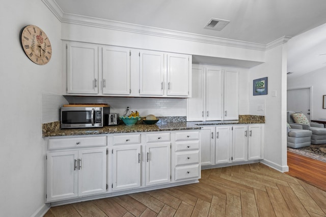 207 Oakwood Cir, Niceville, FL 32578 - kitchen featuring stainless steel microwave, decorative backsplash, white cabinetry, dark stone counters, and crown molding
