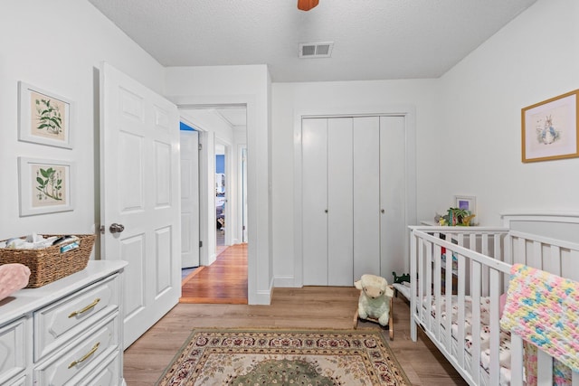207 Oakwood Cir, Niceville, FL 32578 - bedroom with a closet, light wood-style floors, a ceiling fan, a crib, and a textured ceiling