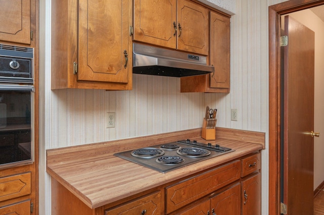 5951 N Meadow Ln, Crestview, FL 32539 - kitchen featuring under cabinet range hood, stainless steel electric stovetop, black oven, brown cabinets, and wallpapered walls