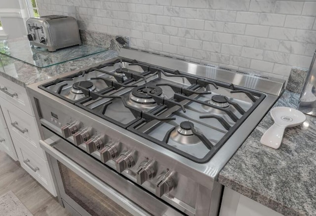 14 Winfield Way, Mary Esther, FL 32569 - kitchen view of stainless steel gas range oven, tasteful backsplash, white cabinetry, stone countertops, and light wood-style flooring