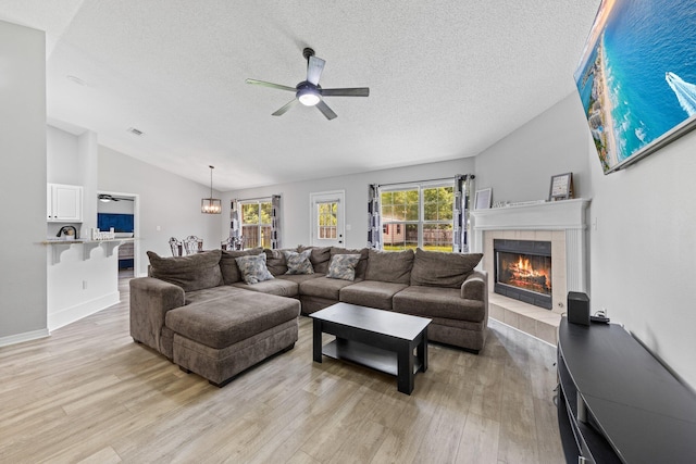 5123 Whitehurst Ln, Crestview, FL 32536 - living room featuring lofted ceiling, ceiling fan, a tiled fireplace, light wood-style flooring, and a textured ceiling