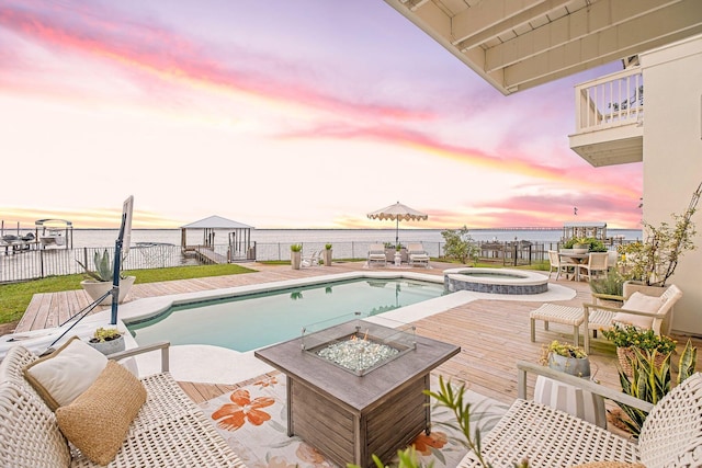 92 Carolyn Ln, Santa Rosa Beach, FL 32459 - pool at dusk with an outdoor fire pit, outdoor dining space, a deck with water view, and a pool with connected hot tub