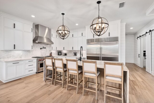 7570 E County Highway 30a, Watersound, FL 32461 - kitchen with wall chimney range hood, high end appliances, a barn door, a chandelier, and light wood-type flooring