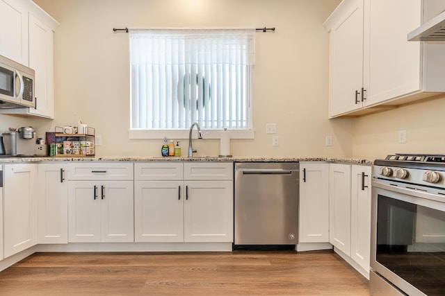 409 Hideaway Ln, Niceville, FL 32578 - kitchen with stainless steel appliances, ventilation hood, white cabinetry, light stone counters, and light wood-style floors