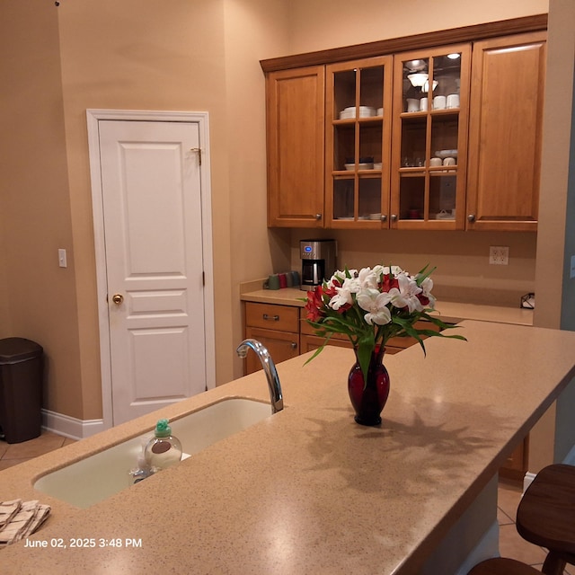 5848 Saratoga Dr, Crestview, FL 32536 - kitchen with brown cabinetry, a sink, glass insert cabinets, and light tile patterned floors