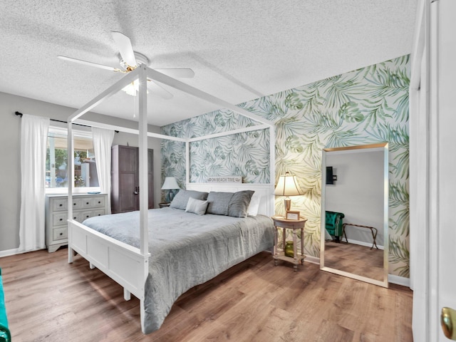 107 Surf Song Ln Unit A1, Miramar Beach, FL 32550 - bedroom with wallpapered walls, a textured ceiling, baseboards, a ceiling fan, and wood finished floors