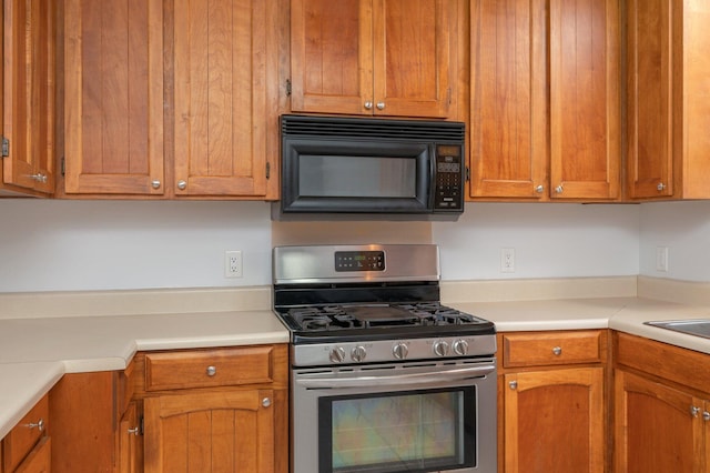 5903 Jack Stokes Rd, Baker, FL 32531 - kitchen with stainless steel gas range oven, black microwave, light countertops, and brown cabinetry