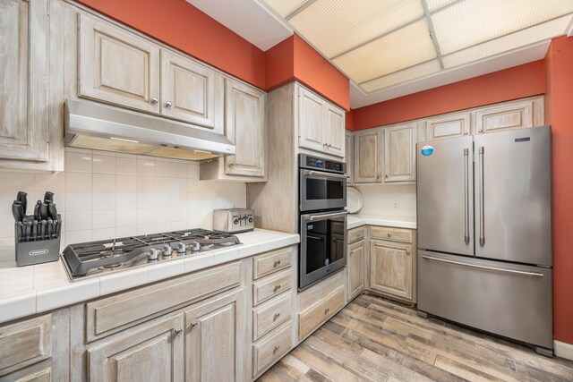9815 US Highway 98 Unit 34, Miramar Beach, FL 32550 - kitchen with stainless steel appliances, under cabinet range hood, tile counters, light wood-style flooring, and decorative backsplash