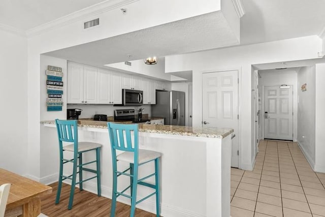 14701 Front Beach Rd Unit 1331, Panama City Beach, FL 32413 - kitchen with stainless steel appliances, a peninsula, white cabinetry, light stone countertops, and a breakfast bar area