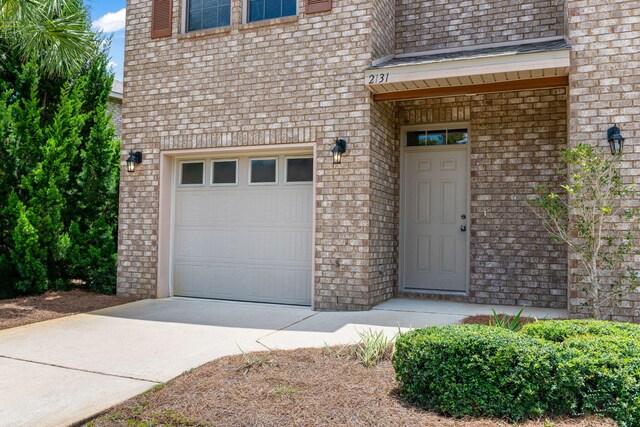 2131 Wilsons Plover Cir, Navarre, FL 32566 - view of exterior entry with an attached garage, concrete driveway, and brick siding