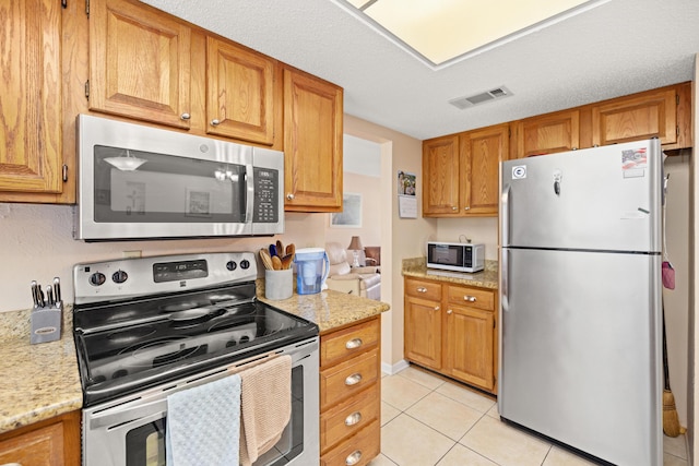 1127 Muirfield Way, Niceville, FL 32578 - kitchen featuring appliances with stainless steel finishes, light tile patterned floors, brown cabinets, and light stone counters