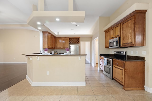 201 Pinque Coat Ct, Crestview, FL 32536 - kitchen featuring appliances with stainless steel finishes, dark countertops, a peninsula, brown cabinetry, and a kitchen bar