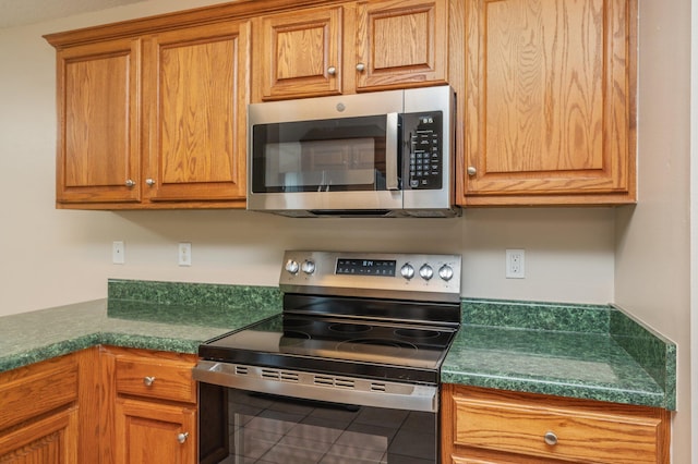 407 Tobago Ct, Crestview, FL 32536 - kitchen with stainless steel appliances, dark countertops, brown cabinetry, and tile patterned floors
