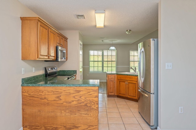 407 Tobago Ct, Crestview, FL 32536 - kitchen featuring appliances with stainless steel finishes, a peninsula, brown cabinets, dark countertops, and a textured ceiling