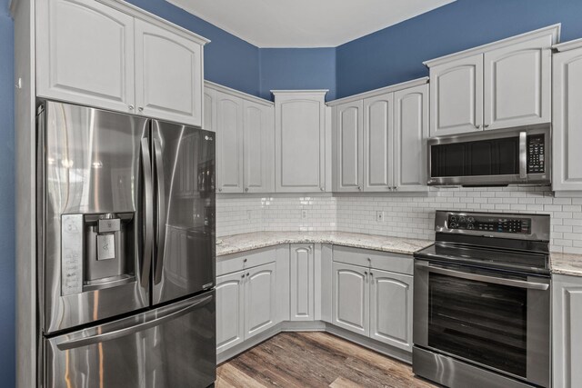 2741 Creeks Edge Ln, Navarre, FL 32566 - kitchen featuring appliances with stainless steel finishes, backsplash, wood finished floors, white cabinets, and light stone countertops