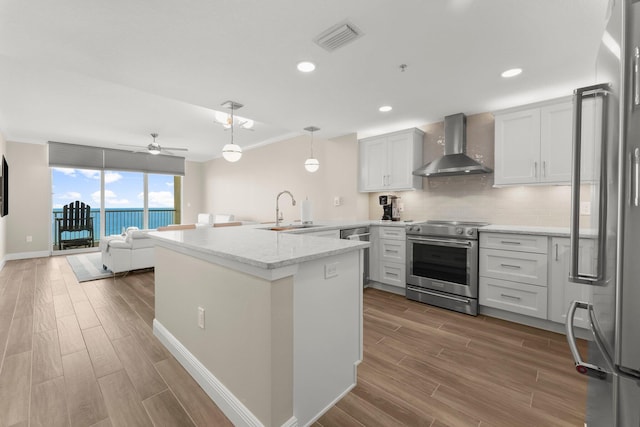 17281 Front Beach Rd Unit 1206, Panama City Beach, FL 32413 - kitchen featuring wall chimney range hood, appliances with stainless steel finishes, wood finished floors, a peninsula, and backsplash