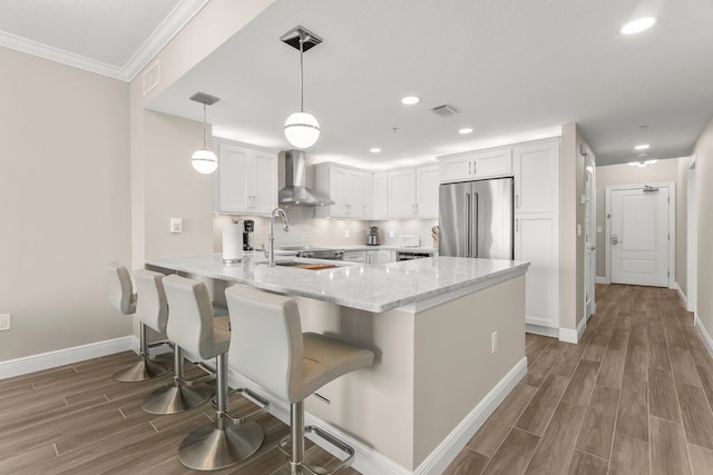 17281 Front Beach Rd Unit 1206, Panama City Beach, FL 32413 - kitchen with high end fridge, wall chimney exhaust hood, a peninsula, white cabinetry, and wood finished floors