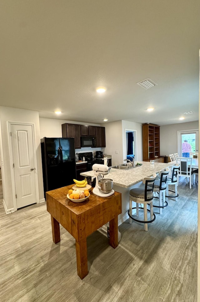 629 Earl Godwin Rd, Freeport, FL 32439 - kitchen featuring black appliances, light wood-type flooring, a breakfast bar, dark brown cabinetry, and a kitchen island with sink