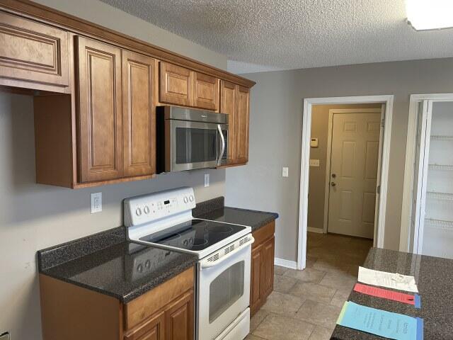 116 Nicole Ln, Crestview, FL 32539 - kitchen featuring stainless steel microwave, white electric range oven, brown cabinets, a textured ceiling, and dark stone counters
