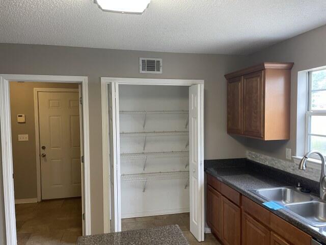 116 Nicole Ln, Crestview, FL 32539 - kitchen featuring dark countertops, a textured ceiling, brown cabinets, and light tile patterned floors