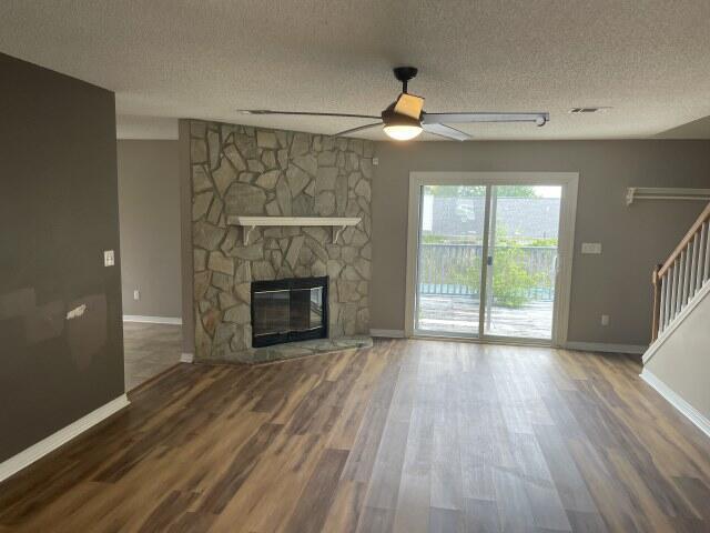 116 Nicole Ln, Crestview, FL 32539 - unfurnished living room featuring a textured ceiling, a ceiling fan, stairs, wood finished floors, and a stone fireplace