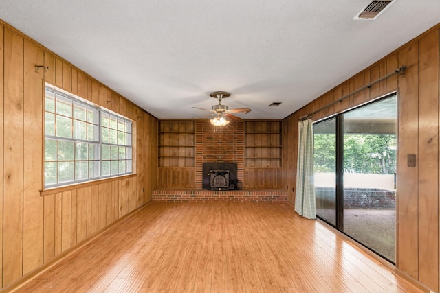 19 Bayview Dr, Shalimar, FL 32579 - unfurnished living room with light wood-type flooring, wooden walls, built in features, a wood stove, and a ceiling fan