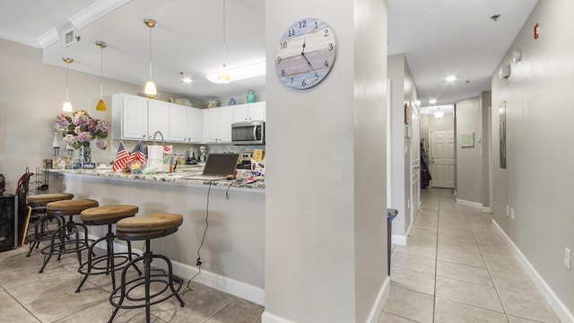 113 SE Brooks St Unit 204, Fort Walton Beach, FL 32548 - kitchen featuring stainless steel microwave, light tile patterned floors, a kitchen breakfast bar, white cabinetry, and crown molding