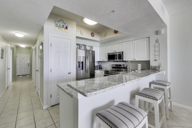 1200 Scenic Gulf Dr Unit B412, Miramar Beach, FL 32550 - kitchen featuring appliances with stainless steel finishes, light tile patterned floors, a textured ceiling, a peninsula, and white cabinetry