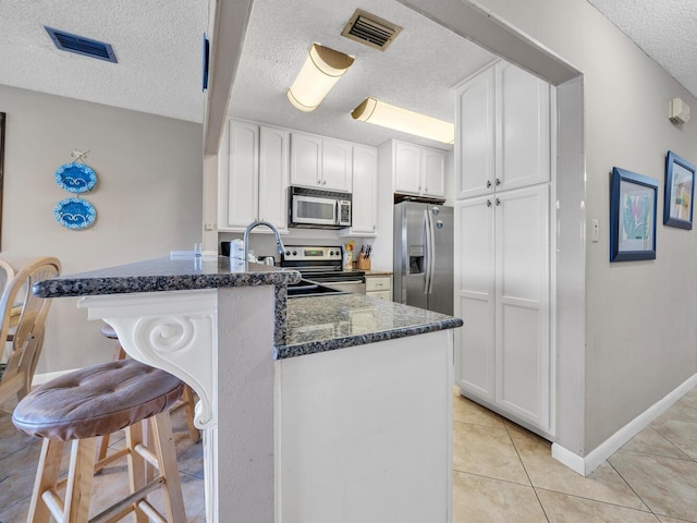 85 S Driftwood Bay Unit 227, Miramar Beach, FL 32550 - kitchen featuring appliances with stainless steel finishes, a textured ceiling, dark stone countertops, white cabinetry, and a peninsula