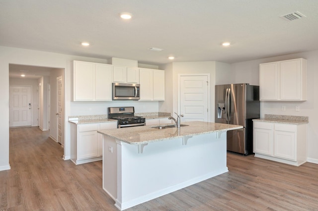 4652 Honor Guard Way, Crestview, FL 32539 - kitchen featuring stainless steel appliances, light wood-type flooring, light stone countertops, an island with sink, and white cabinets
