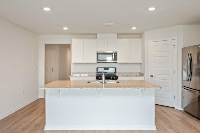 4652 Honor Guard Way, Crestview, FL 32539 - kitchen featuring stainless steel appliances, light wood finished floors, a kitchen island with sink, light stone countertops, and a kitchen breakfast bar