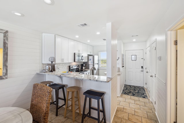 23011 Front Beach Rd Unit E-20, Panama City Beach, FL 32413 - kitchen with appliances with stainless steel finishes, light stone counters, white cabinets, a breakfast bar, and a peninsula