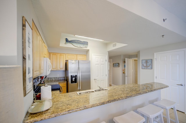 112 Seascape Blvd Unit 210, Miramar Beach, FL 32550 - kitchen with stainless steel fridge, light brown cabinetry, a peninsula, white microwave, and light stone counters