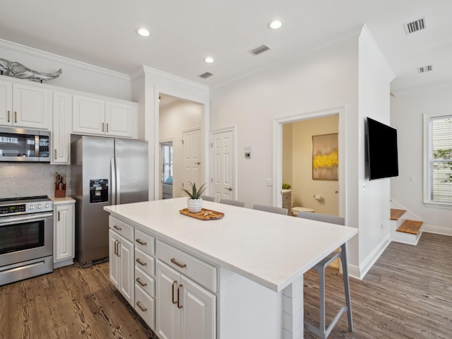 221 Seacrest Beach Blvd E, Seacrest, FL 32461 - kitchen featuring appliances with stainless steel finishes, ornamental molding, white cabinetry, dark wood-style floors, and a kitchen bar