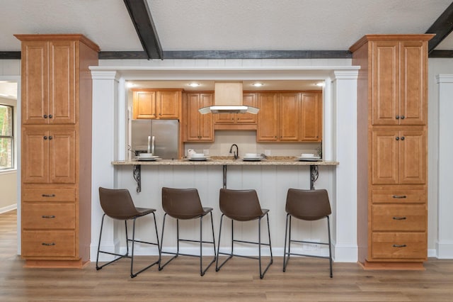 6060 Bud Moulton Rd, Crestview, FL 32536 - kitchen with stainless steel fridge, wall chimney range hood, a kitchen breakfast bar, light wood-style flooring, and beamed ceiling
