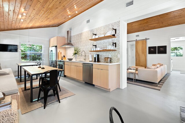 41 E Grove Ave, Santa Rosa Beach, FL 32459 - kitchen featuring a barn door, stainless steel appliances, light brown cabinetry, wall chimney exhaust hood, and finished concrete floors