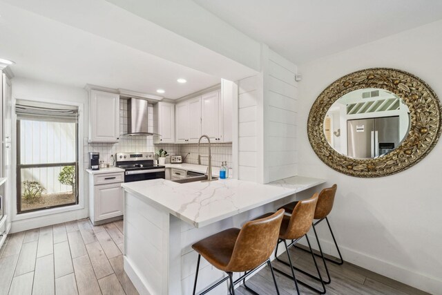736 Sandpiper Pl Unit 10525, Miramar Beach, FL 32550 - kitchen with wall chimney exhaust hood, electric range, light wood-type flooring, decorative backsplash, and a breakfast bar