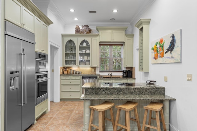 176 Rue Martine, Miramar Beach, FL 32550 - kitchen with appliances with stainless steel finishes, a peninsula, cream cabinetry, dark stone counters, and ornamental molding