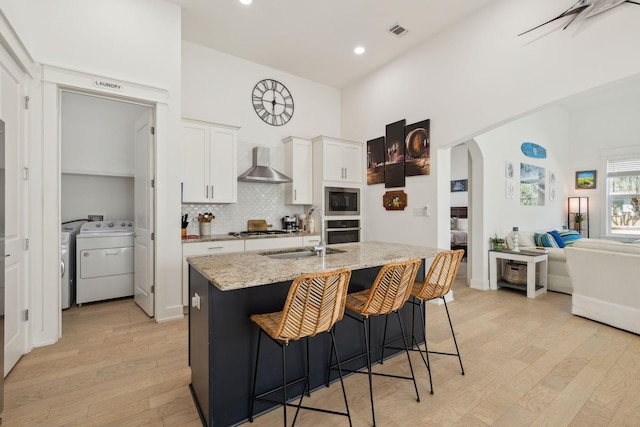 234 Grande Pointe Cir, Inlet Beach, FL 32461 - kitchen with wall chimney range hood, stainless steel appliances, light wood-type flooring, washing machine and dryer, and white cabinets
