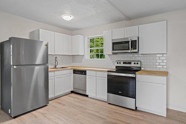 1023 W Webster Dr, Pensacola, FL 32505 - kitchen featuring appliances with stainless steel finishes, butcher block counters, light wood finished floors, tasteful backsplash, and a textured ceiling