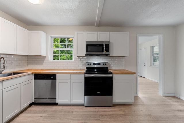 1023 W Webster Dr, Pensacola, FL 32505 - kitchen featuring appliances with stainless steel finishes, wood counters, light wood-style flooring, white cabinetry, and decorative backsplash