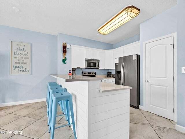9900 S Thomas Dr Unit 1604, Panama City Beach, FL 32408 - kitchen featuring stainless steel appliances, light tile patterned floors, white cabinetry, a kitchen breakfast bar, and light countertops