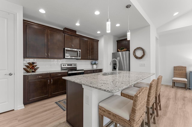 8668 Shell Sink Dr, Panama City Beach, FL 32413 - kitchen featuring appliances with stainless steel finishes, light wood-style flooring, a kitchen breakfast bar, decorative backsplash, and dark brown cabinetry
